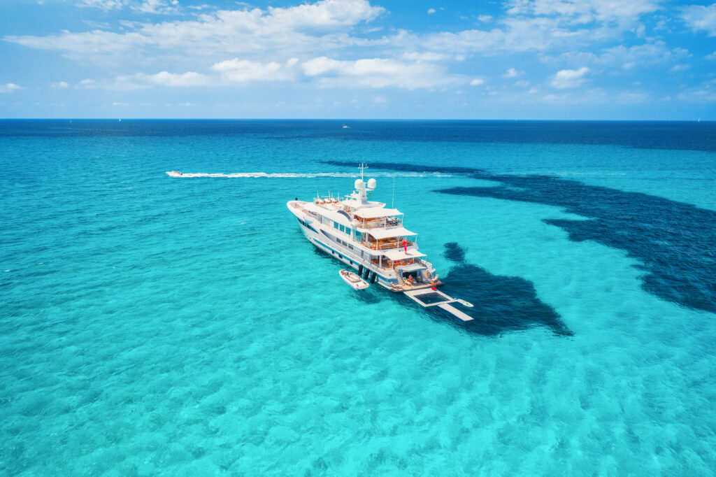 Bateau sur la côte azur des îles Baléares. Vue aérienne d'un bateau flottant avec des personnes dans une mer transparente lors d'une journée ensoleillée en été. Vue de dessus depuis un drone. Paysage marin avec des yachts de luxe en mouvement dans la baie.